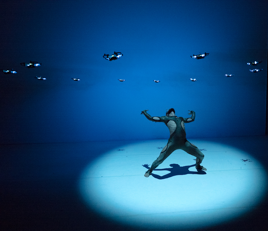 Foto van een voorstelling van David Middendorp; je ziet ene danser met boven hem allerlei drones in de lucht