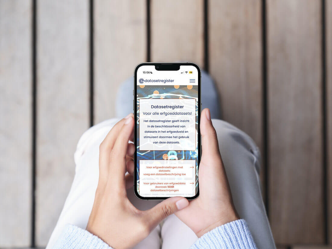 Iemand die zit houdt met beide handen een mobieltje vast. Opde achtergrond zie je een houten vloer