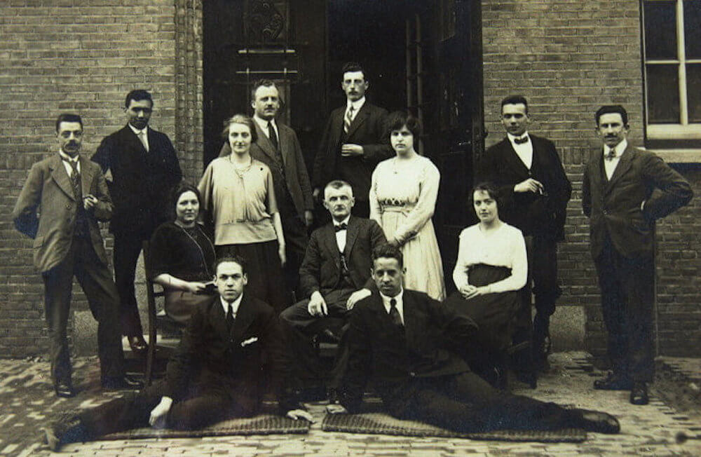 Een zwartwitfoto van een negen leraren en drie leraressen voor een schoolgebouw, eind 18e eeuw, begin 19-eeuw